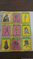 Photo showing nine Star Wars Empire Strikes Back trading cards in a binder sleeve, featuring characters such as Darth Vader, Han Solo, Luke Skywalker, C-3PO, and others.