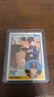 Photo of 1983 Nolan Ryan baseball card in protective sleeve, showing front with pitching action and portrait.