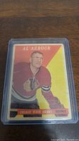 Single 1958-59 Topps Al Arbour hockey card in protective plastic sleeve on wooden surface.