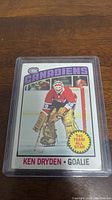 Photo of the 76-77 Topps Ken Dryden hockey card in a protective sleeve showing front side with player image and team branding.