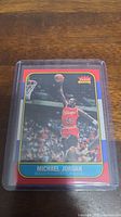 Front of Michael Jordan 1986 Fleer rookie basketball card reprint showing action image of Jordan in red Chicago Bulls jersey going for a dunk.
