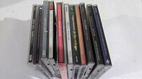 View of 11 CDs arranged standing on their spines showing case edges and some album art edges.