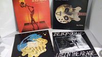 Full view of all four Be-Bop Deluxe album covers placed flat: Sunburst Finish, Futurama, orange cover with saxophone, and Live in the Air Age double album.