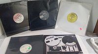 Lot of five 12-inch vinyl records in a variety of black and white paper sleeves, arranged standing and lying flat on a surface.