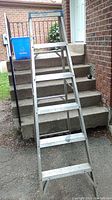Full view of aluminum step ladder leaning against concrete stairs in outdoor setting.