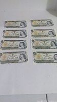 Eight 1937 Canadian one dollar bills arranged flat on a white surface, showing the front side with Queen Elizabeth II's portrait and decorative borders.
