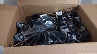 Open cardboard box filled with over 150 new sunglasses loose, showing various frame styles and lens colors including black and gold frames with tags visible.