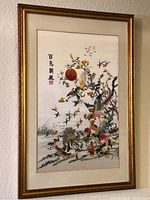 Full view of framed embroidered silk artwork hung on wall showing various birds, flowers, and Asian characters.