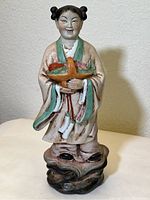 Full view of the 16-inch tall Chinese porcelain woman figurine standing on a rocky base, holding a flower basket.