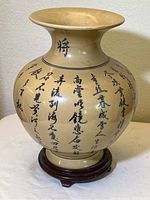 Front angle view of tan Chinese ceramic vase showing full body with hand-painted black calligraphy characters and wooden stand base.