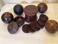 Set showing four carved wood balls, small covered dish with a base, a cylindrical carved holder, and six coasters.