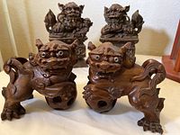 Pair of carved wood Fu dogs viewed from side and front showing detailed carving and facial features.