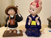 Pair of Hakata-style dolls including a seated girl doll in a blue kimono and a standing Buddhist monk figurine with a small dog on base