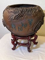 Side view of the pottery bowl showing sculpted bark details, turquoise colored markings, and wooden stand underneath
