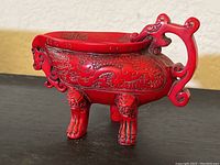 Side view of red coral color dragon cup showing detailed dragon carving, ornate handle, and three legs.