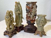 Group photo showing four soapstone carved items on wooden and stone stands