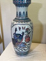Full view of tall porcelain vase with peacock and floral painted design.