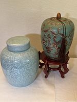 Photo showing two large covered ceramic jars, one decorated and on stand, the other crackled glaze finish
