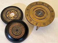 Two compasses displayed side by side, one brass on tripod stand with engraved rotating rings, the other in a Chinese-style wood box with decorative lid and face.