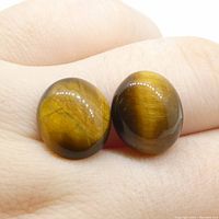 Two oval cabochon Tigers Eye gemstones held on a finger showing color and reflective chatoyancy characteristic of Tigers Eye.