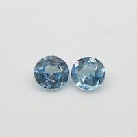 Two round blue zircon gemstones placed side by side on a white background to show size, cut, and color.