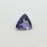 Close-up photo of the trillion cut violet-blue iolite gemstone on a plain background showing facets and color.