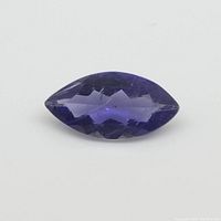 Close-up image of a marquise cut violet-blue iolite gemstone on a neutral background showing faceted surfaces and color.