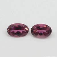 Close-up of two oval faceted pink tourmaline gemstones with visible clarity and color, displayed on a white background.