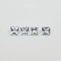 Four square blue aquamarine gemstones placed in a row on a white background showing the size and cut.