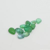 Ten pear cabochon green emerald gemstones arranged on white background showing color and shape.
