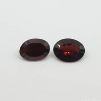 Two oval almandine garnet gemstones placed flat on a white background showing their faceted cuts and deep red color.