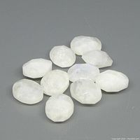 Ten oval-shaped white rainbow moonstone gems with blue flash on a gray background.