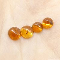 Four round cabochon orange hessonite garnet gemstones resting on a palm, showing translucency and internal inclusions.