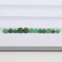 Front view of 12 green emerald sphere beads lined up in a row on a white tray, showing size and color variations