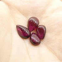Four pear cabochon rhodolite garnet gemstones held in a hand showing color and size.