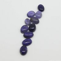 Ten oval cabochon iolite gemstones arranged on white background showing violet-blue shades and polish.