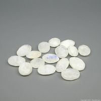 Sixteen faceted oval rainbow moonstones with white base and blue flash, displayed on gray background.