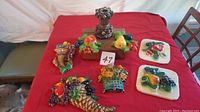 Overview of all seven chalkware pieces on red cloth showing variety of fruit and cornucopia designs, including small pedestal figurine.