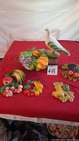 Full overview of all chalkware wall pieces on red fabric background, showing bird figure and multiple fruit clusters