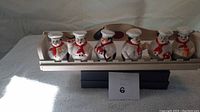 Front view of the spice rack holding six chef ceramic spice containers, all lined up evenly on the wooden rack.