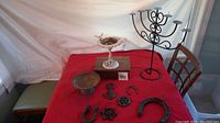 Full view of metalware assortment on red cloth including menorah, metal bowls, hooks, horseshoes and gear pieces
