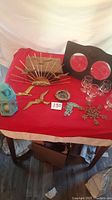 Wide shot of lot on red cloth table showing all decorative items including metal wall décor, wooden frame, glasses, and lantern
