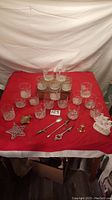 Photo showing a total of 18 clear etched glasses and various metal bar tools arranged on a red cloth.