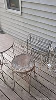 Photo showing the round table with wire legs, stool with round seat, magazine rack, and plant stand on a wooden deck.