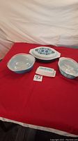 Four-pieces of vintage Pyrex glassware including casserole dishes and butter dish arranged on red cloth background