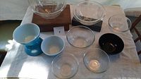 All bowls arranged on white towel, various sizes and colors including blue pedestal bowls and clear glass bowls.