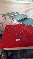 Set of three metal stacking tables with decorative turquoise tops showing circular and wavy line patterns, nested on red cloth.