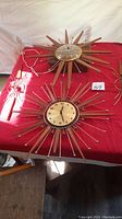 Two starburst wall clocks and sconce parts arranged on red fabric