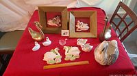 Full lot of swan figurines on red tablecloth showing all items, two framed plaques, swan planter, brass swans, small ceramic and glass swans