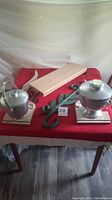 Two hammered metal ice buckets with lids and handles on pink marble bases with wooden charcuterie board and green metal wall brackets on red tablecloth